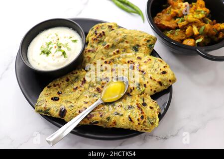 Ein Essen namens Methi Paratha oder Methi Thepla ist ein indisches Frühstücksgericht mit Quark und einem Löffel voller Desi Ghee serviert. Stockfoto