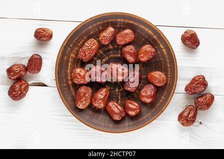 Mehrere süße getrocknete ziziphus-Beeren mit einer Keramikplatte auf einem Holztisch, Nahaufnahme, Draufsicht. Stockfoto