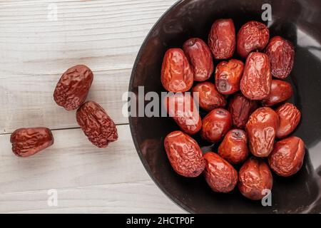 Mehrere süße getrocknete ziziphus-Beeren mit einer Keramikplatte auf einem Holztisch, Nahaufnahme, Draufsicht. Stockfoto