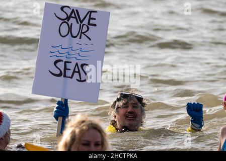 Jubilee Beach, Southend on Sea, Essex, Großbritannien. 1st Januar 2022. Die Menschen haben sich für wohltätige Zwecke in die kalten Gewässer der Themsemündung gebracht, um Gelder für die lokale Niederlassung der Royal National Lifeboat Institution zu sammeln. Mitglieder der RNLI waren aus Sicherheitsgründen zur Verfügung, viele der Schwimmer trugen Kostüme in schicken Kleidern. Rund 300 Personen nahmen daran Teil. Schwimmer mit dem Schild „Save Our Seas“, in Bezug auf die jüngste Verschmutzung der Kanalisation Stockfoto