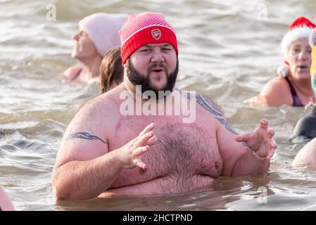 Jubilee Beach, Southend on Sea, Essex, Großbritannien. 1st Januar 2022. Die Menschen haben sich für wohltätige Zwecke in die kalten Gewässer der Themsemündung gebracht, um Gelder für die lokale Niederlassung der Royal National Lifeboat Institution zu sammeln. Mitglieder der RNLI waren aus Sicherheitsgründen zur Verfügung, viele der Schwimmer trugen Kostüme in schicken Kleidern. Rund 300 Personen nahmen daran Teil. Großer übergewichtiger Mann im Wasser mit Wollmütze, der nach kaltem Schock keuchte Stockfoto