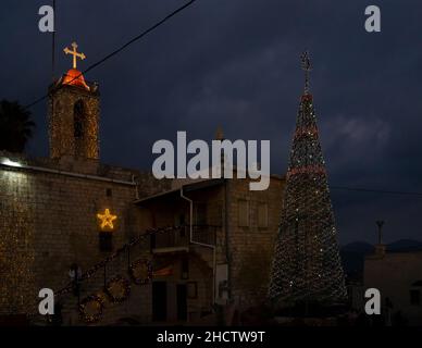 Mi'ilia, Israel - 25th. Dezember 2021: Die Kirche und ein weihnachtsbaum, geschmückt zu weihnachten in dem arabisch-christlichen Dorf Mi'ilia, Israel, am twil Stockfoto