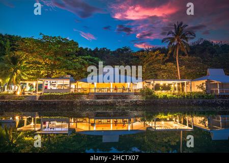 Ein See mit Spiegelung eines weißen Bungalows an der Küste gegen Palmen bei Sonnenuntergang Stockfoto