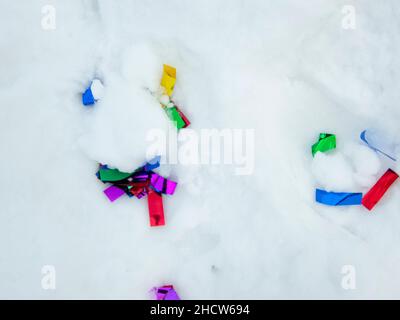 Konfetti im Schnee. Bunte Konfetti im Schnee nach einer festlichen Party zu Weihnachten oder Neujahr. Verschmutzung der Natur durch Plastik Stockfoto