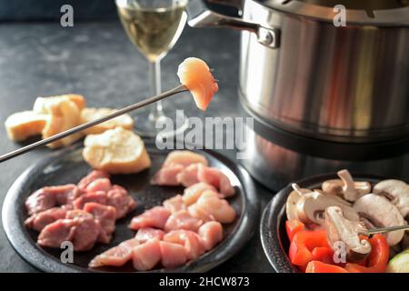 Heißes Öl-Fondue mit Fleischstücken und Gemüse, in einem Topf mit brutzelndem Fett gebraten werden, geselliges festliches Abendessen oft auf Partys serviert, ausgewählt Stockfoto