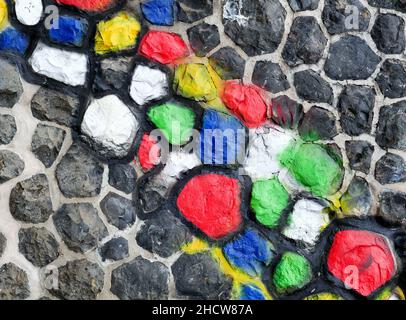 Steinwand mit Muster.einzelne Steine einer Steinwand sind mit hellen Farben bemalt Stockfoto