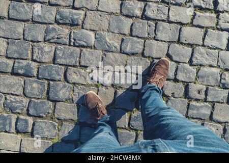 Der junge Mann steht auf Kopfsteinpflaster, einem hohen Fußbauch oder einem flortrait, persönlich pessektiv von oben. Stockfoto