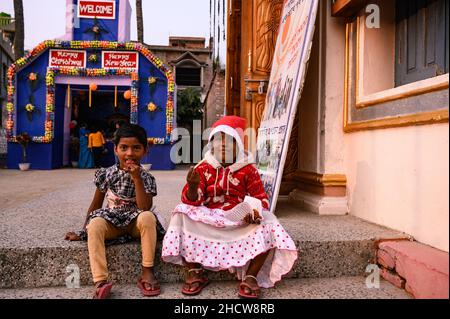 In Haulia, Westbengalen, Indien, feiern Kinder aus verschiedenen fernen Dörfern in einer kleinen Kirche das Weihnachtsfest und spielen vor einem großen Jesus Christus-Foto. Stockfoto