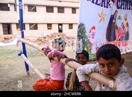 In Haulia, Westbengalen, Indien, feiern Kinder aus verschiedenen fernen Dörfern in einer kleinen Kirche das Weihnachtsfest und spielen vor einem großen Jesus Christus-Foto. Stockfoto