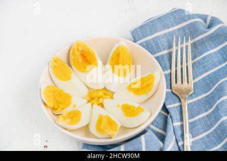 Eier, in Scheiben geschnittene gekochte Eier auf weißem Teller auf Holzgrund oder Tisch für ein gesundes Frühstück. Ketogenes Frühstück auf Holzoberfläche oder Hintergrund Stockfoto