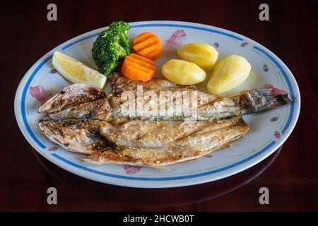 Gegrillter Seebarsch kletterte mit gebackenen Kartoffeln und Gemüse in Teller auf den Tisch. Traditionelles portugiesisches Gericht. Stockfoto