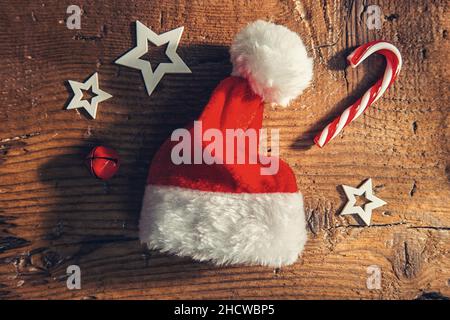 weihnachtsmann Hut mit Zuckerrohr und Dekoration auf einem Holzbrett, Frohe Weihnachten Hintergrund Stockfoto