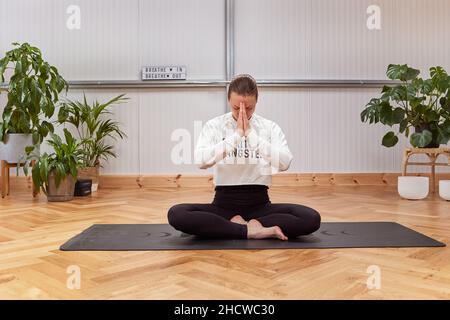 Entspannt barfuß weibliche Augen schließen und Gyan Mudra gestikulieren, während sie in Lotus-Pose auf der Matte sitzen und während der Yoga-Sitzung im Lichtstudio meditieren Stockfoto