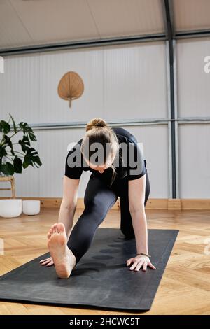 Entspannt barfuß weibliche Augen schließen und Gyan Mudra gestikulieren, während sie in Lotus-Pose auf der Matte sitzen und während der Yoga-Sitzung im Lichtstudio meditieren Stockfoto