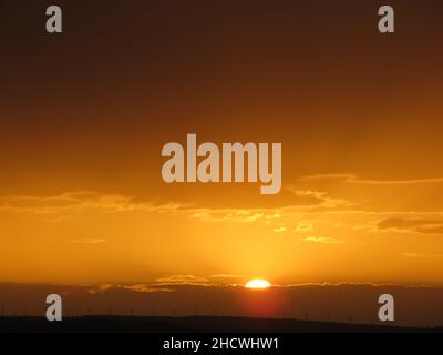 Wunderschöner Orang-Sonnenuntergang-Himmel mit der untergehenden Sonne hinter Bergen und Wolken Stockfoto