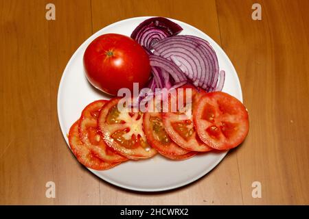 Selektive Konzentration auf Tomatenscheiben und violette Zwiebel in Scheiben auf einem runden weißen Teller Stockfoto