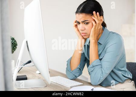 Gelangweilte weibliche Angestellte, die an der Rezeption vor dem Computer saß, wegschaute und sich traurig fühlte. Nachdenkliche junge Frau hat keine Inspiration für die Arbeit, fühlt sich mangelnden Schlaf und Müdigkeit Stockfoto