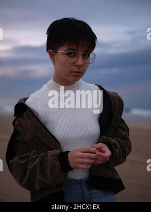 Transgender Frau, die in warmen Kleidern vor dem Strand posiert und die Hände hält Stockfoto