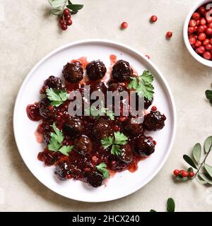 Fleischbällchen mit Cranberry-Sauce auf dem Teller auf hellem Steingrund. Draufsicht, flach liegend Stockfoto