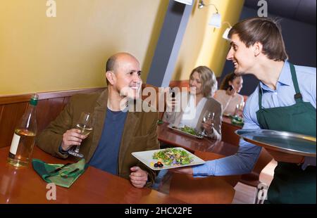 Kellner, der ältere männliche Gäste im Café bedient Stockfoto