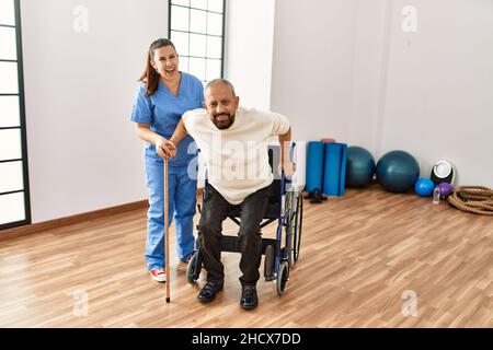 Älterer Mann, der auf dem Rollstuhl sitzt, wird von einer Altenpflegerin unterstützt, behinderter reifer Mann, der Hilfe beim Aufstehen bekommt Stockfoto