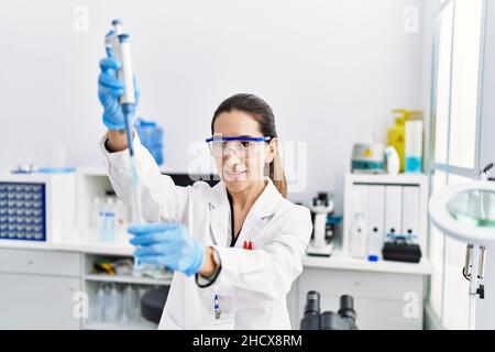 Junge hispanische Frau trägt Wissenschaftlerin Uniform mit Pipette im Labor Stockfoto