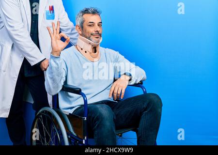 Schöner Mann mittleren Alters mit grauen Haaren auf Rollstuhl trägt Halsband lächelnd positive tun ok Zeichen mit Hand und Fingern. Erfolgreiche expressi Stockfoto