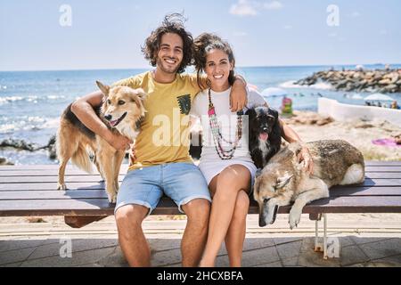 Mann und Frau Paar lächeln selbstbewusst und umarmen sich am Meer mit Hunden Stockfoto