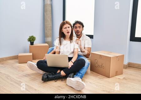 Junges Paar, das zu Hause einen Laptop benutzt, sieht schockiert aus, sieht skeptisch und sarkastisch aus, überrascht mit offenem Mund Stockfoto