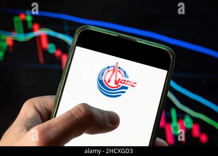 In dieser Abbildung ist das chinesische Öl- und Gasunternehmen China National Offshore Oil Corporation oder CNOOC Group abgebildet, das Logo auf einem Smartphone mit einem wirtschaftlichen Börsenindex im Hintergrund. Stockfoto