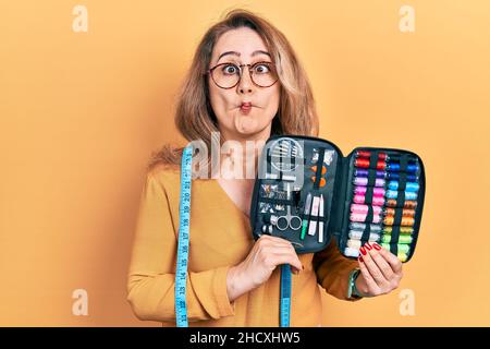 Kaukasische Frau mittleren Alters trägt Maßband mit Näh-Kit, das Fische Gesicht mit Mund und Augen schielt, verrückt und komisch. Stockfoto