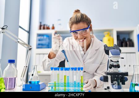 Junge blonde Frau trägt Wissenschaftlerin Uniform mit Pipette im Labor Stockfoto