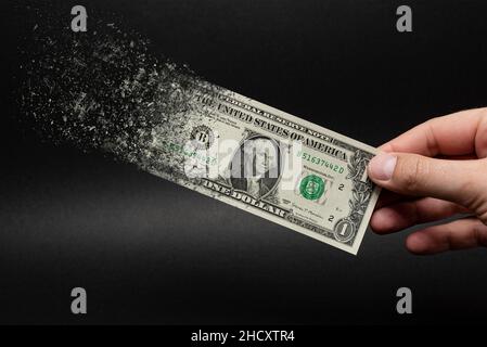 Inflation, Dollar-Hyperinflation mit schwarzem Hintergrund. Ein Dollarschein wird in die Hand eines Mannes auf schwarzem Hintergrund gesprüht. Das Konzept der Decreadi Stockfoto