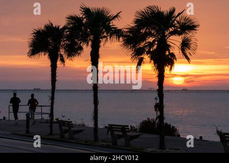 Sonnenaufgang am Morgen des 1. Januar 2022 in Southend on Sea, Essex, Großbritannien. Zwei Jogger, die an Palmen entlang der Strandpromenade laufen Stockfoto