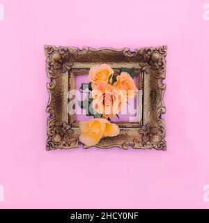 Frische orangefarbene Rosen kommen aus einem goldenen Retro-Barockrahmen auf einem pastellrosa Hintergrund. Romantisches Blumenkonzept zum Valentinstag. Hochzeitsfeier Stockfoto