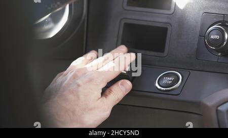 Nahaufnahme der Hand, die den Start- oder Stoppknopf des Fahrzeugs drückt, um den Motor auszuschalten. Blick in ein luxuriöses, teures Fahrzeug, Fahrer hält an Stockfoto