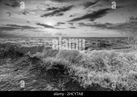 Ein Ozean Seascape Sunset Sky mit Einer detaillierten Wolkenlandschaft als Eine Welle stürzt Shore in Schwarz-Weiß-Bildformat Stockfoto