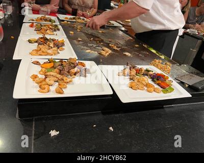 Im japanischen Teppanyaki-Restaurant warten Gäste auf den Koch. In Echtzeit werden Gerichte aus Gemüse, Rindfleisch, Fisch, Garnelen und Huhn zubereitet. Stockfoto