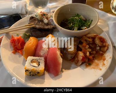 Ein großer weißer Teller mit gemischtem Surf- und Turf-Essen inklusive Steak und Sushi. Farbenfrohe Sushi-Brötchen, Ceviche-Salat, Rindersteak, gegrillter Fisch und Green Sal Stockfoto