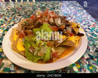 Leckere Salsa Nachos großes Gericht auf einem weißen Teller. Chips und Käse mit Guacamole, Bohnen, Tomaten, Zwiebeln und Hühnerstücken. Stockfoto