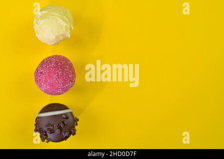 Schokoladenbonbons oder Pralinen auf einem gelben pastellfarbenen Hintergrund. Schokoladenpralinen auf gelbem Hintergrund mit Kopierfläche. Flach liegend, Draufsicht. Stockfoto
