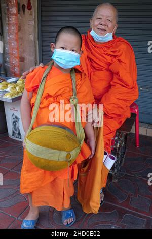 Ein thailändischer buddhistischer Mönch und ein 8-jähriger junger Novize unter seiner Obhut, ausgestattet mit der üblichen Almosenschale, posiert fröhlich für die Kamera; Bangkok, Thailand Stockfoto