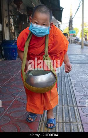 Ein junger, 8 Jahre alter Mönch oder Novize während der traditionellen Mönchsalmrunde, trat am frühen Morgen mit seiner Almosenschale auf; Bangkok, Thailand Stockfoto