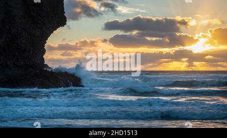 Riesige Wellen krachen bei Sonnenuntergang gegen die Felsen am Piha Beach, Auckland, Neuseeland. Stockfoto