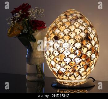 Eine wunderschöne ovale Lampe mit Details vor weißem Hintergrund in einem dunklen Raum neben einem Blumentopf. Stockfoto