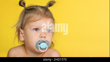 Porträt von niedlichen kaukasischen Kind Kind Mädchen von 2 Jahren mit Schnuller im Mund auf gelbem Hintergrund mit Kopieplatz Stockfoto