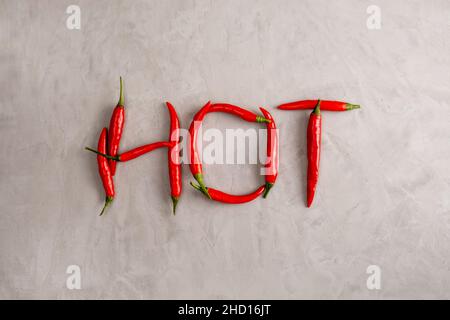 HOT Lettering ist mit Schoten von roten Chili-Paprika auf grauem Hintergrund mit Gips-Textur ausgekleidet. Gewürze, gesundes Essen. Selektiver Fokus. Blick von der Stockfoto