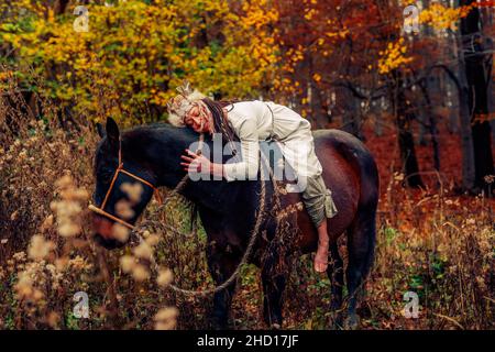 Schamane Frau in Herbstlandschaft mit ihrem Pferd. Stockfoto