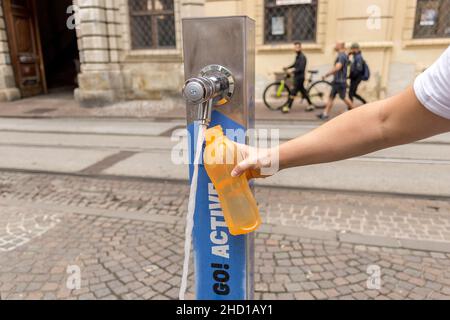 Graz, Österreich - 23. August 2021: Frau füllt ihre Wasserflasche mit frischem Trinkwasser in einem öffentlichen Brunnen in der Grazer Innenstadt auf Stockfoto