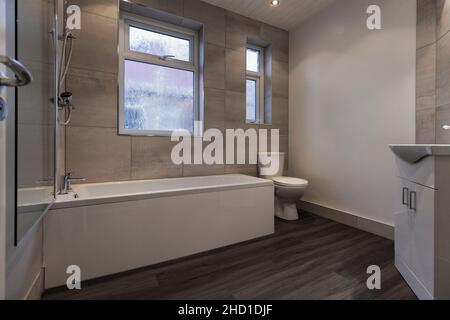 Modernes Badezimmer mit Schminkbereich, großen weißen Barrington-Fliesen, grauem und weißem LVT-Vinylboden, Duschbad, Duschabtrennwand und Toilette Stockfoto